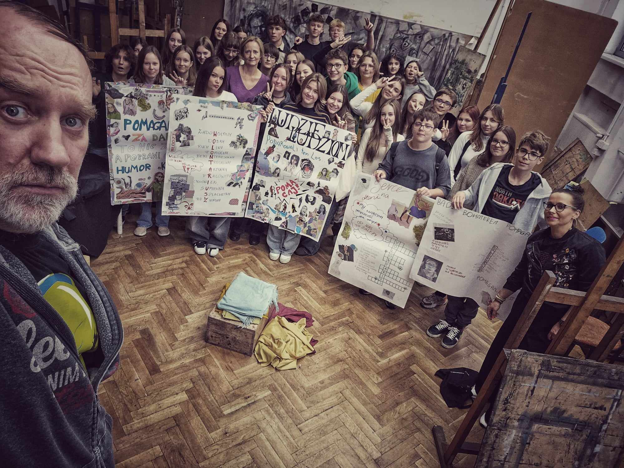 Grupa ludzi trzymająca kolorowe plakaty. Na pierwszym planie po lewej stronie mężczyzna z szarą brodą i w szarej bluzie 